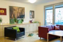 Bild zeigt den Tagesraum der Station KJP1 mit Sofa uns Sessel, Spielzeugen, Fenster und Bild eines Elefanten an der Wand