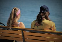 Das Bild zeigt zwei Jugendliche von hinten, die auf einer Bank sitzen und reden. 